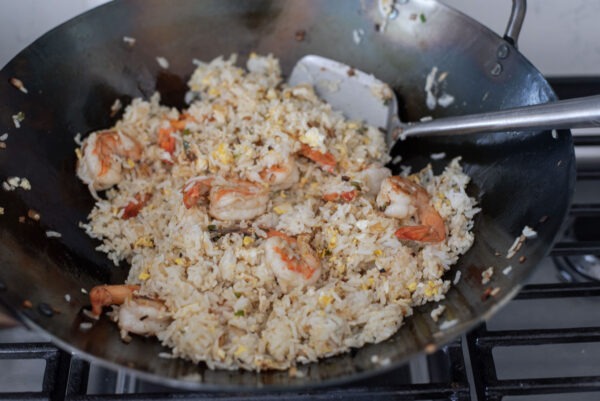 Rice is added to shrimp and savory ingredients in a wok.