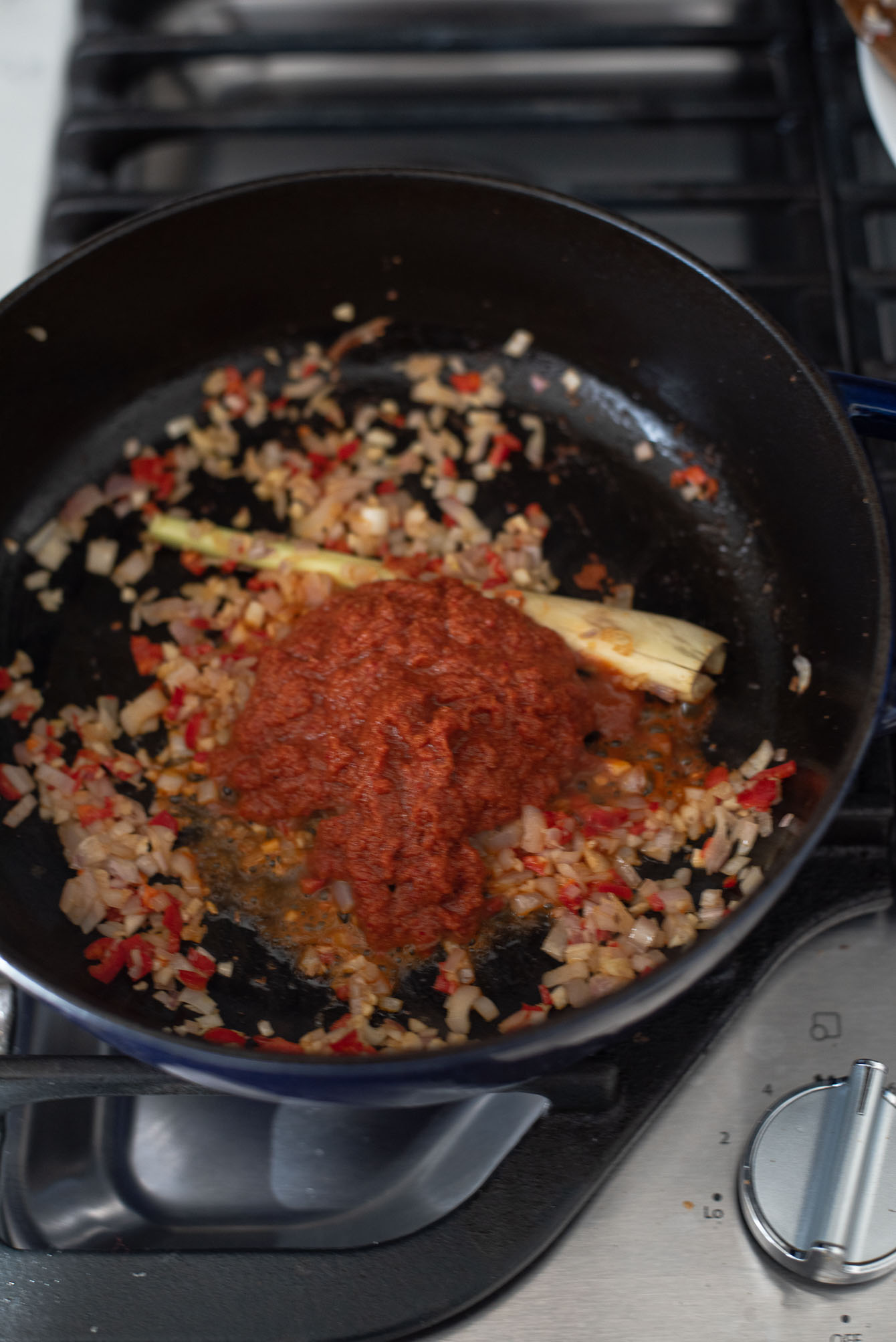 Thai red curry paste added to savory ingredients in a pot.