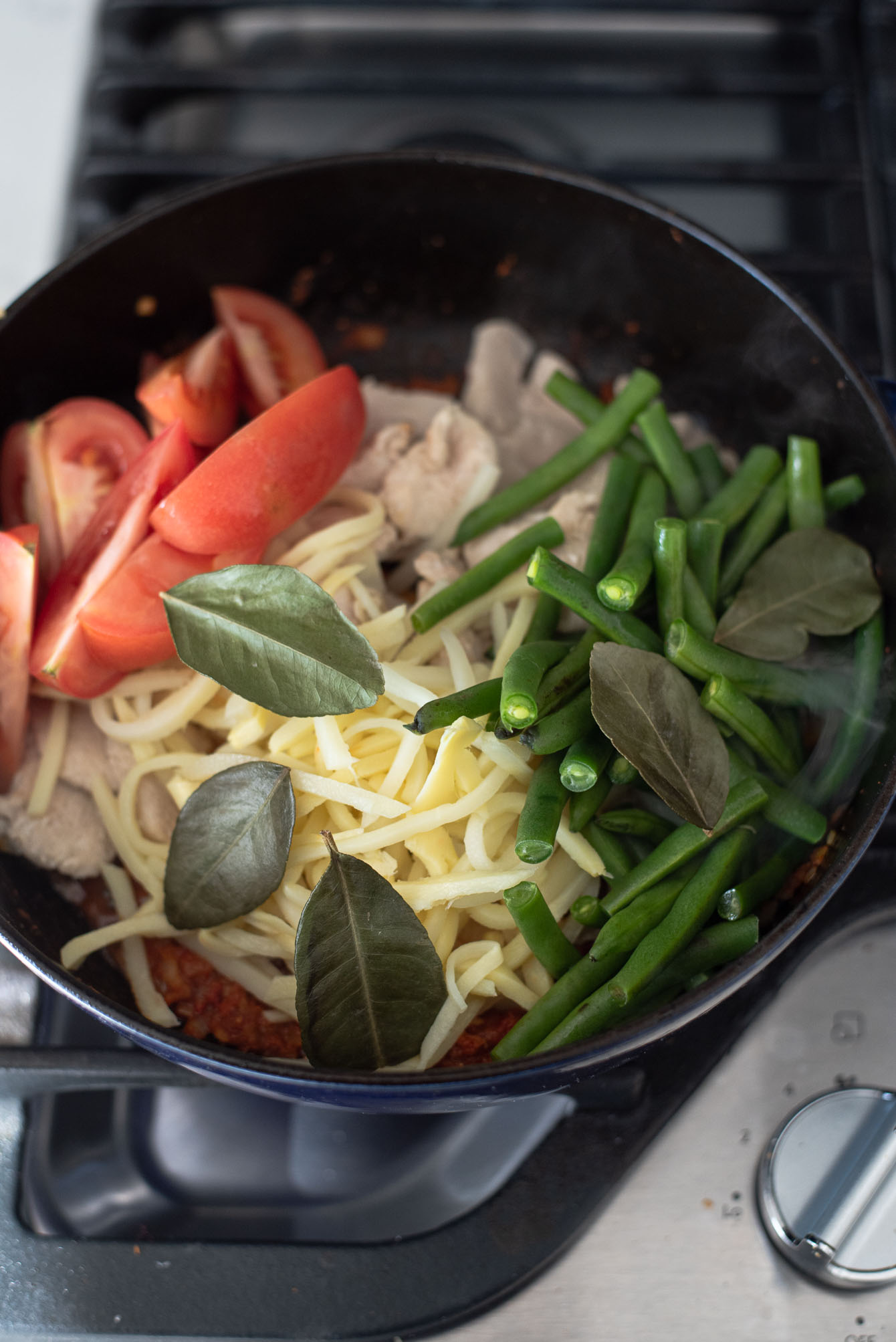 Vegetables added to Thai red curry paste in a pot.