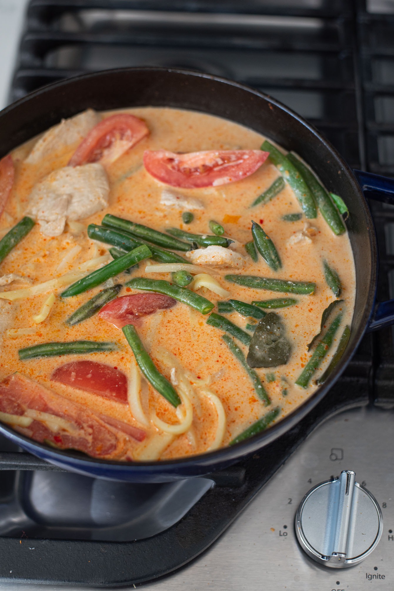 Coconut milk is added to Thai red curry chicken and vegetables in a pot.
