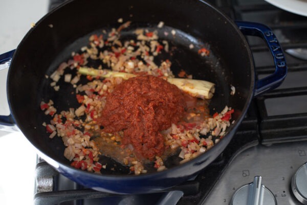 Thai red curry paste is added to fried savory ingredients in a pot.