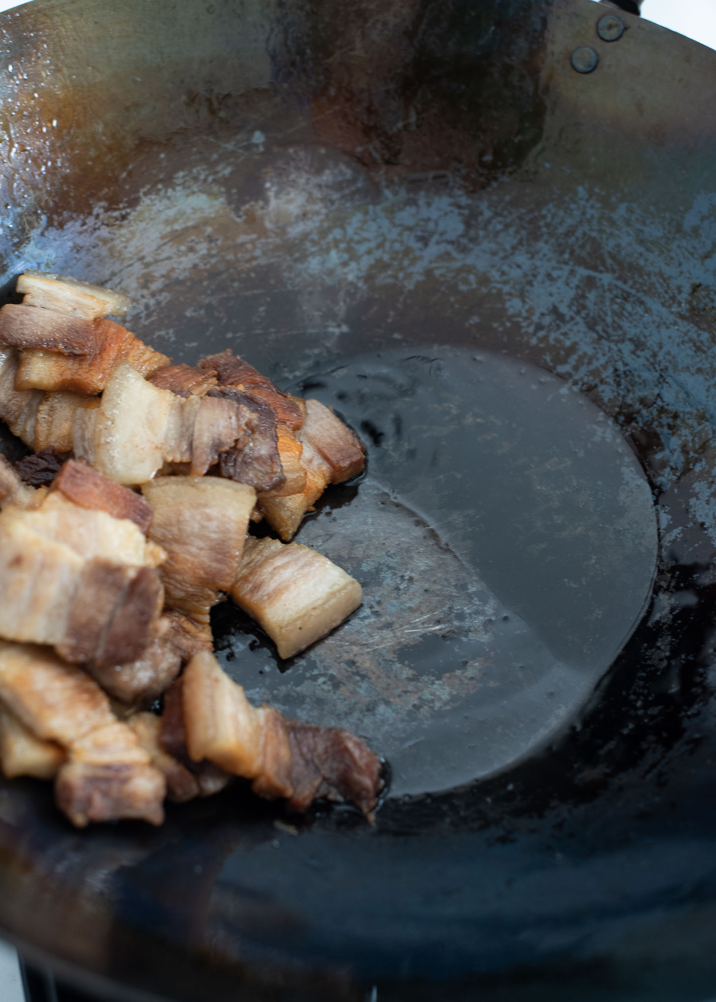 Fat from the cooking pork belly is rendered in a wok.