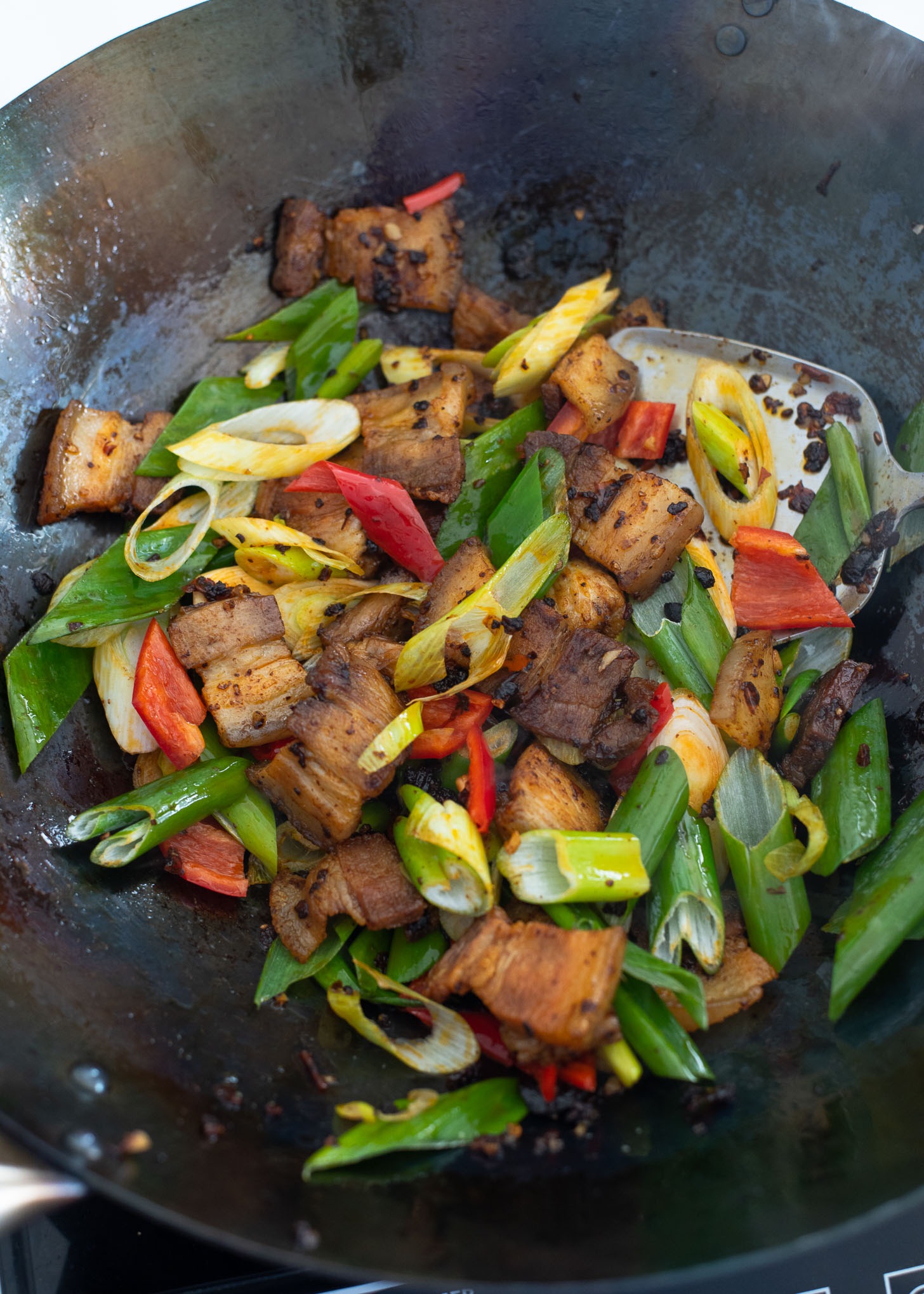 Asian leek and red chili are added to twice cooked pork to finish cooking.
