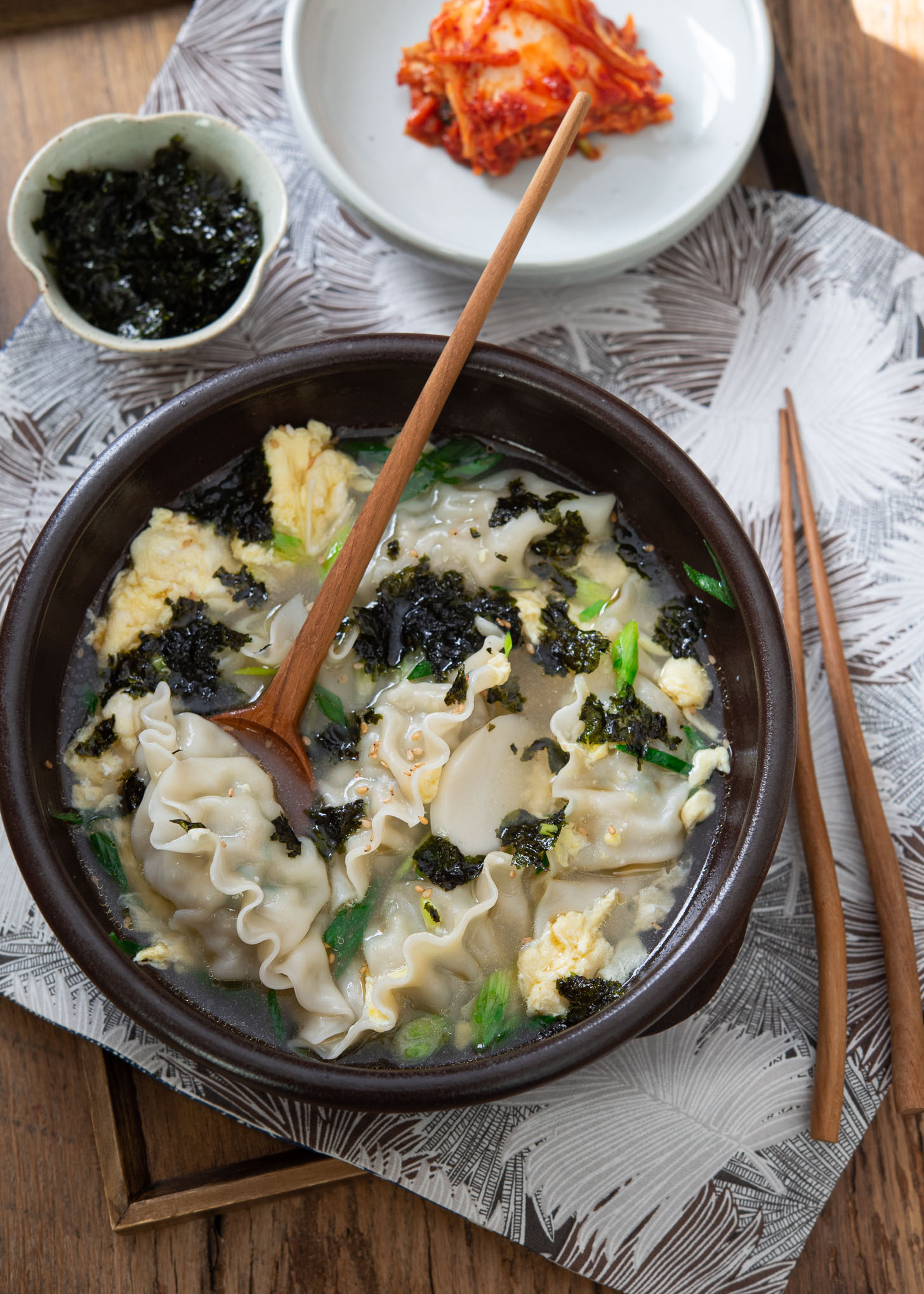 A spoon is holding a piece of mandu in a bowl of dumpling soup.