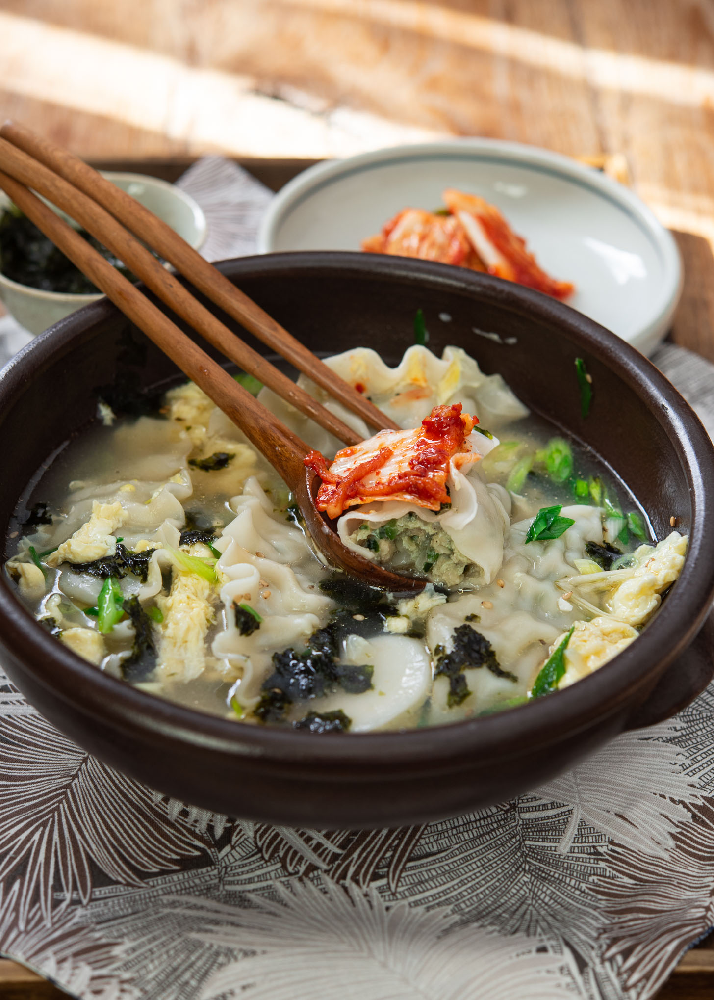 Korean dumpling soup is served with kimchi in a bowl.