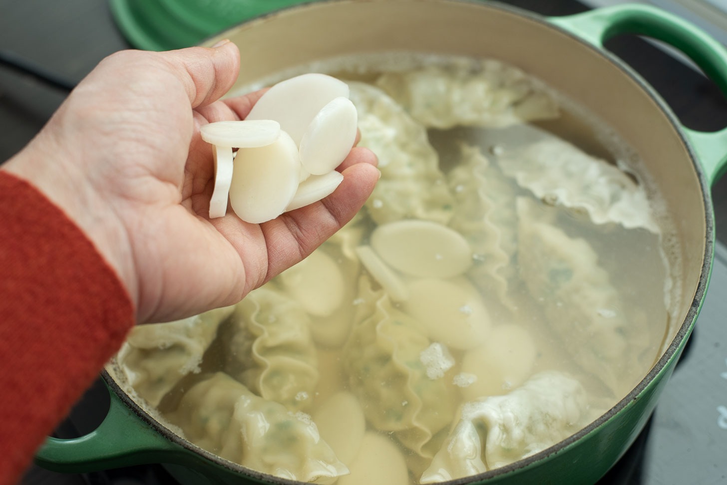 Frozen dumplings and rice cake rounds are added to the soup base in a pot.
