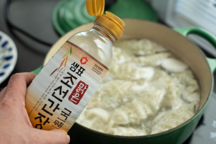 Korean soup soy sauce is added to dumpling soup in a pot.