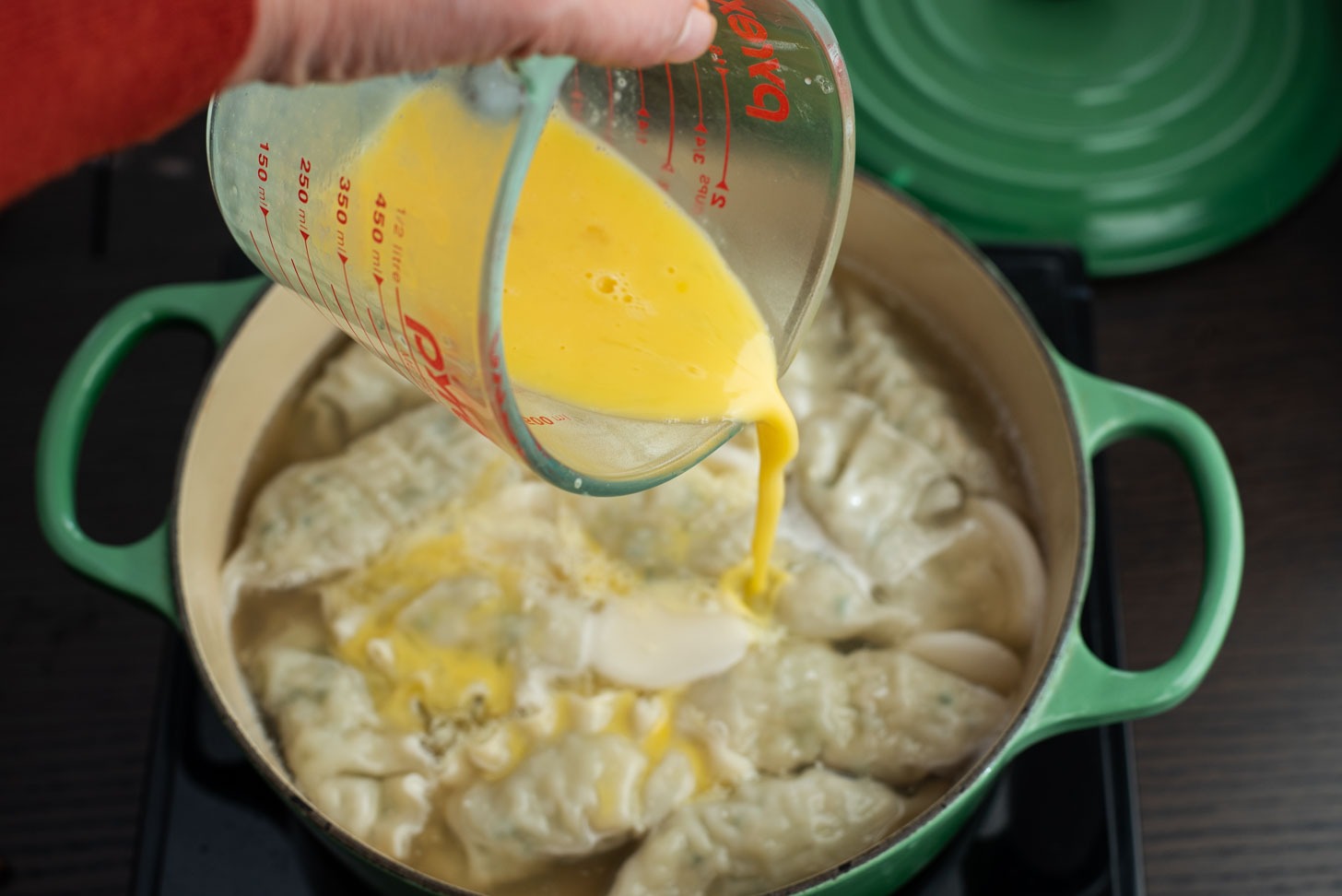 Beaten eggs are added to the simmering dumpling soup in a pot.