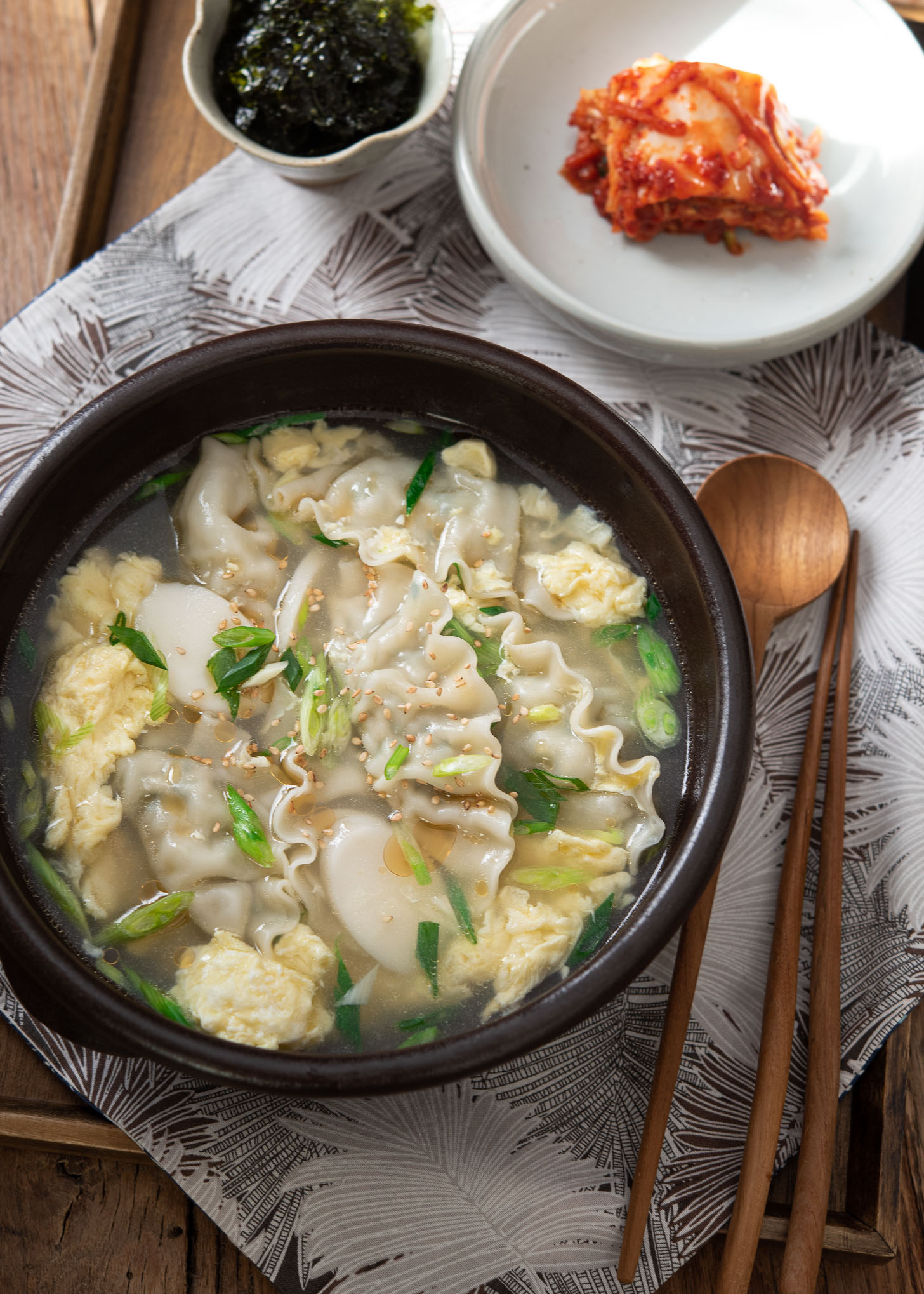 A bowl of mandu guk, Korean dumpling soup, is served with kimchi.