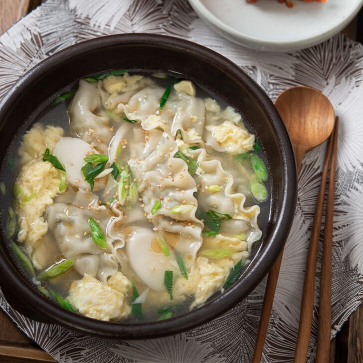 A bowl of mandu guk, Korean dumpling soup, is served with kimchi.