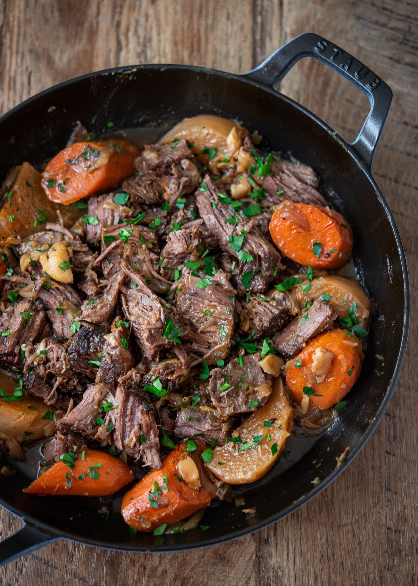 Spiced beef pot roast with onion, carrot, and turnip is arranged in a braising pan.