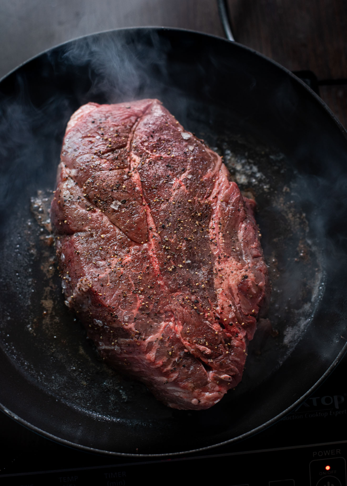 A piece of beef chuck is seasoned and getting seared in a pan.