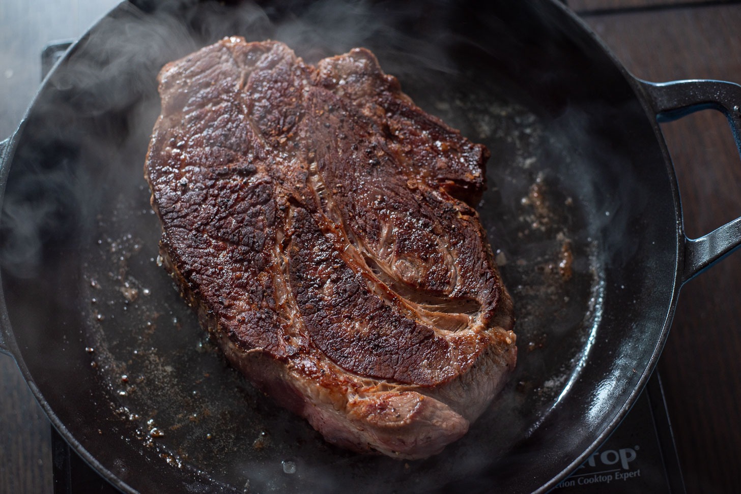 Seasoned beef chuck is searing in a pan until browned and caramelized.