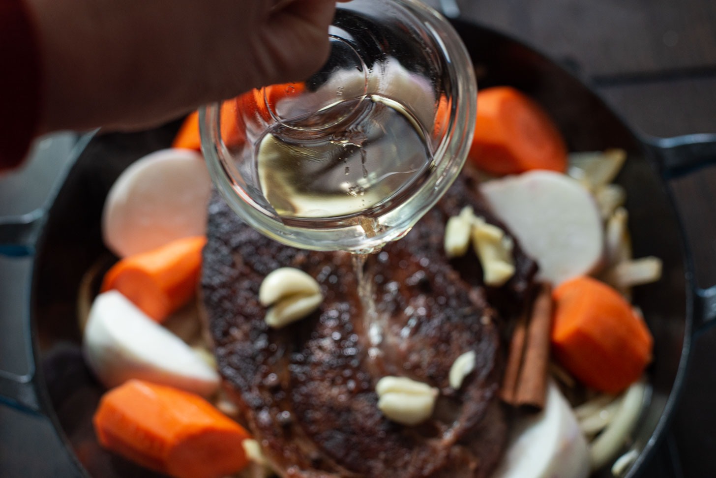 Vinegar is being added to the beef, carrot, turnip in a braising pan.