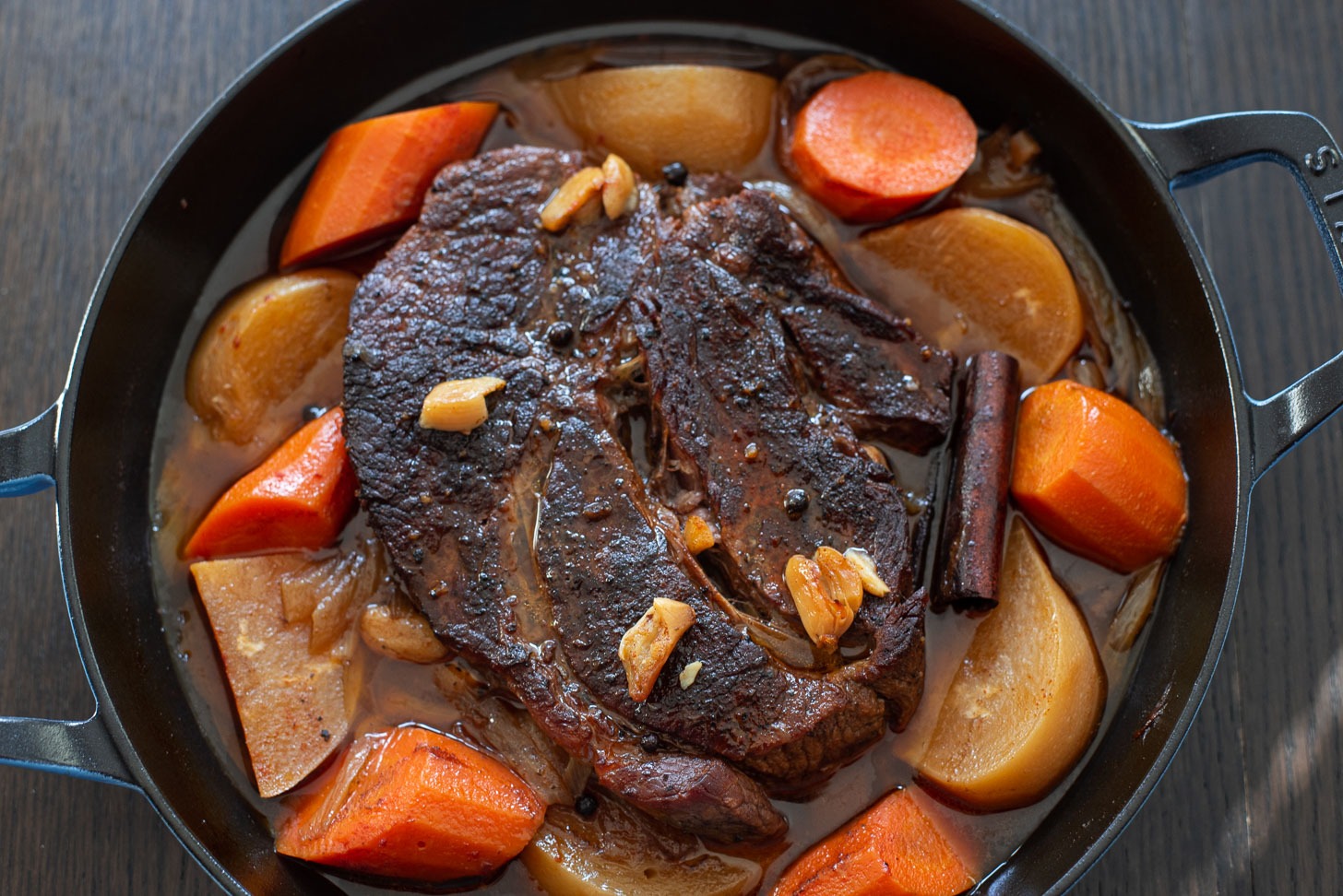 Spiced beef pot roast with onion, carrot, turnip is presented in a braising pan.
