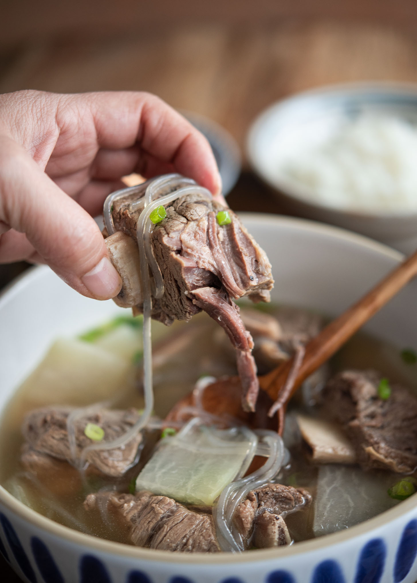 A hand is holding a piece of galbitang short rib over the bowl of soup.