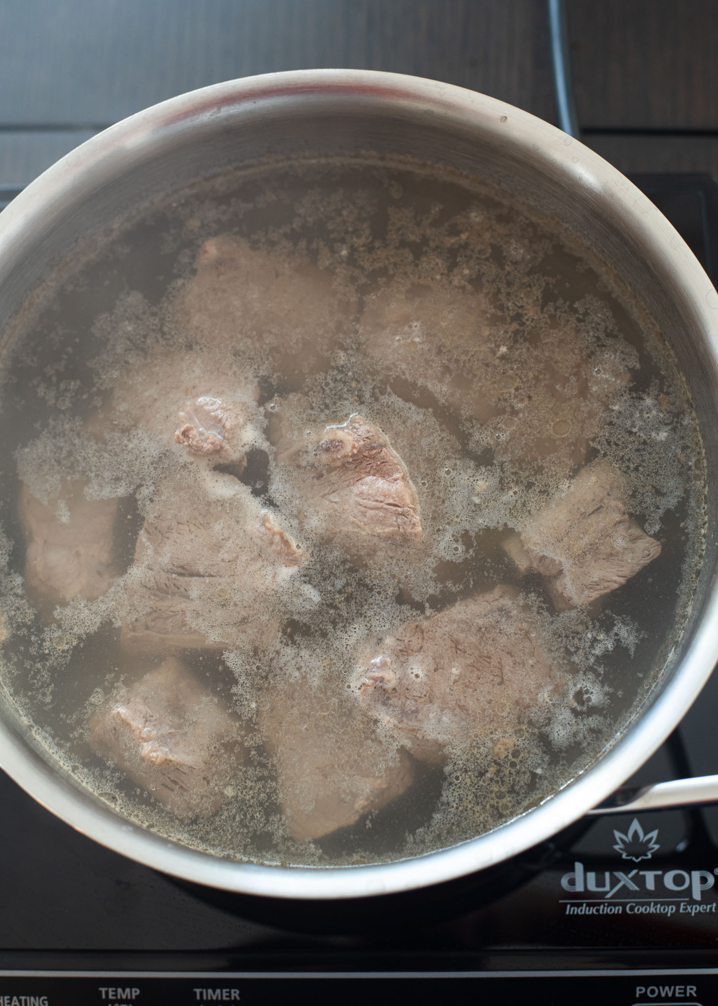 Beef short ribs are parboiling in a pot.