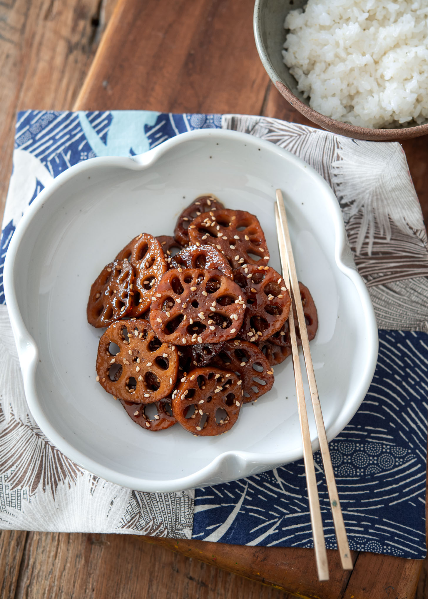 Korean braised lotus root is served in a white plate with chopsticks on the side.