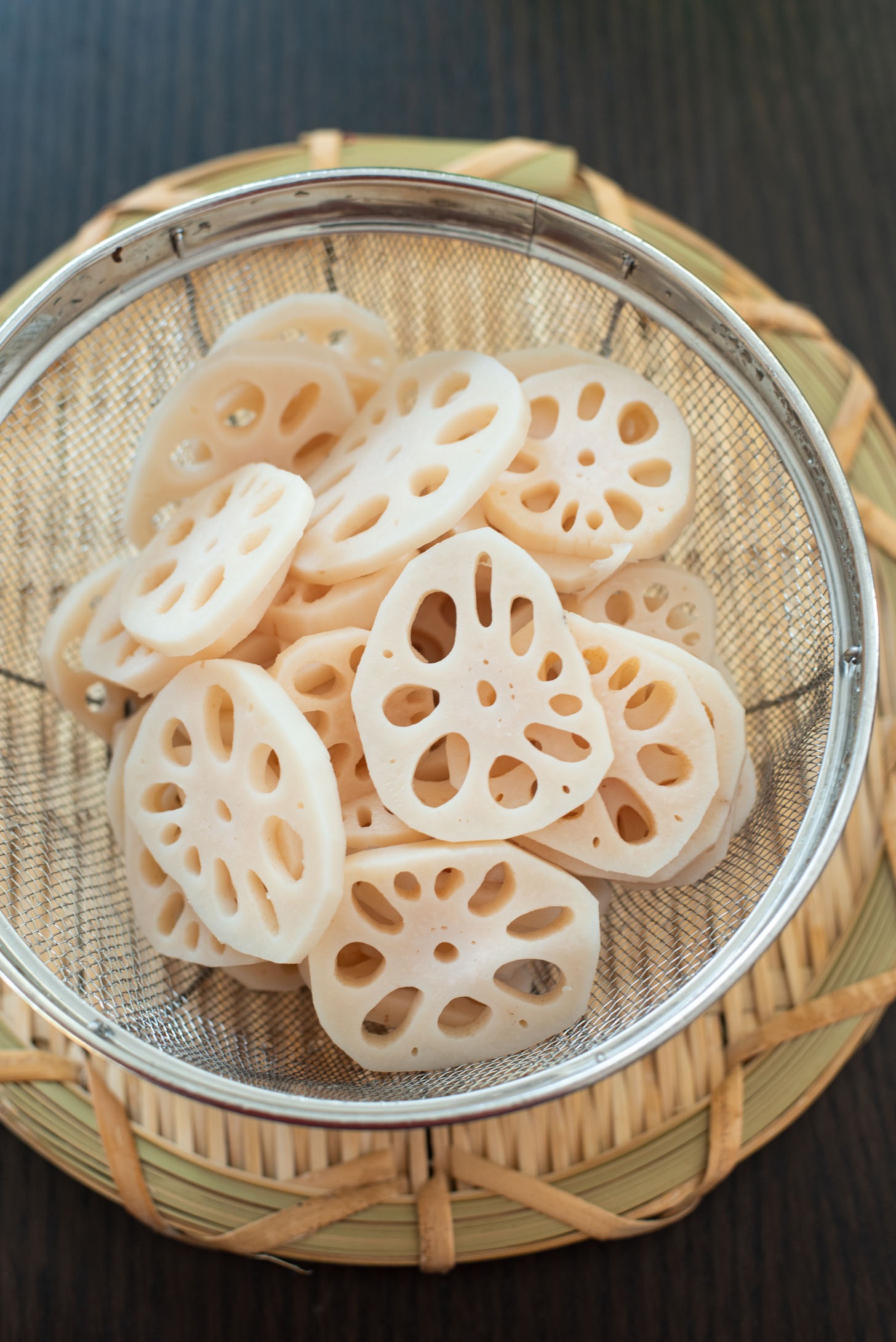 Boiled lotus root slices are drained in a colander.