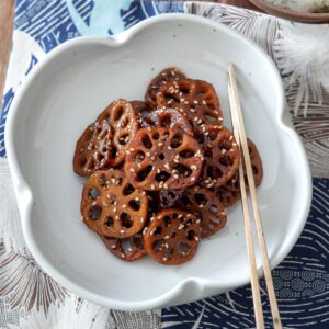 Korean braised lotus root is served in a white plate with chopsticks on the side.
