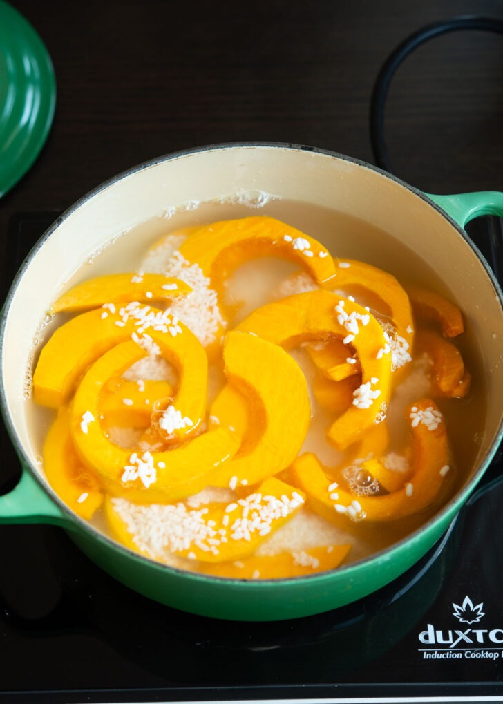 Pumpkin slices and sweet rice is combined with water in a soup pot.