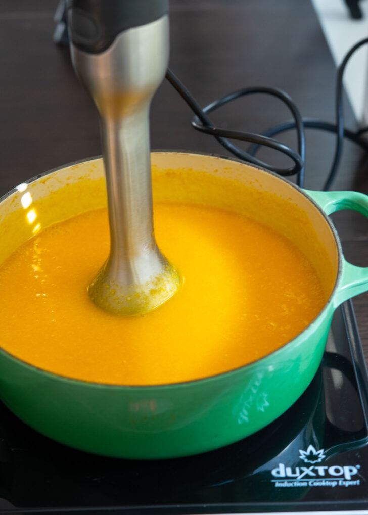 An immersion blender is pureeing the pumpkin porridge right in the pot.