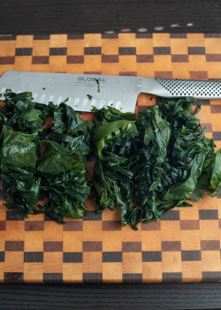 Rehydrated seaweed cut with a knife on a wooden board.