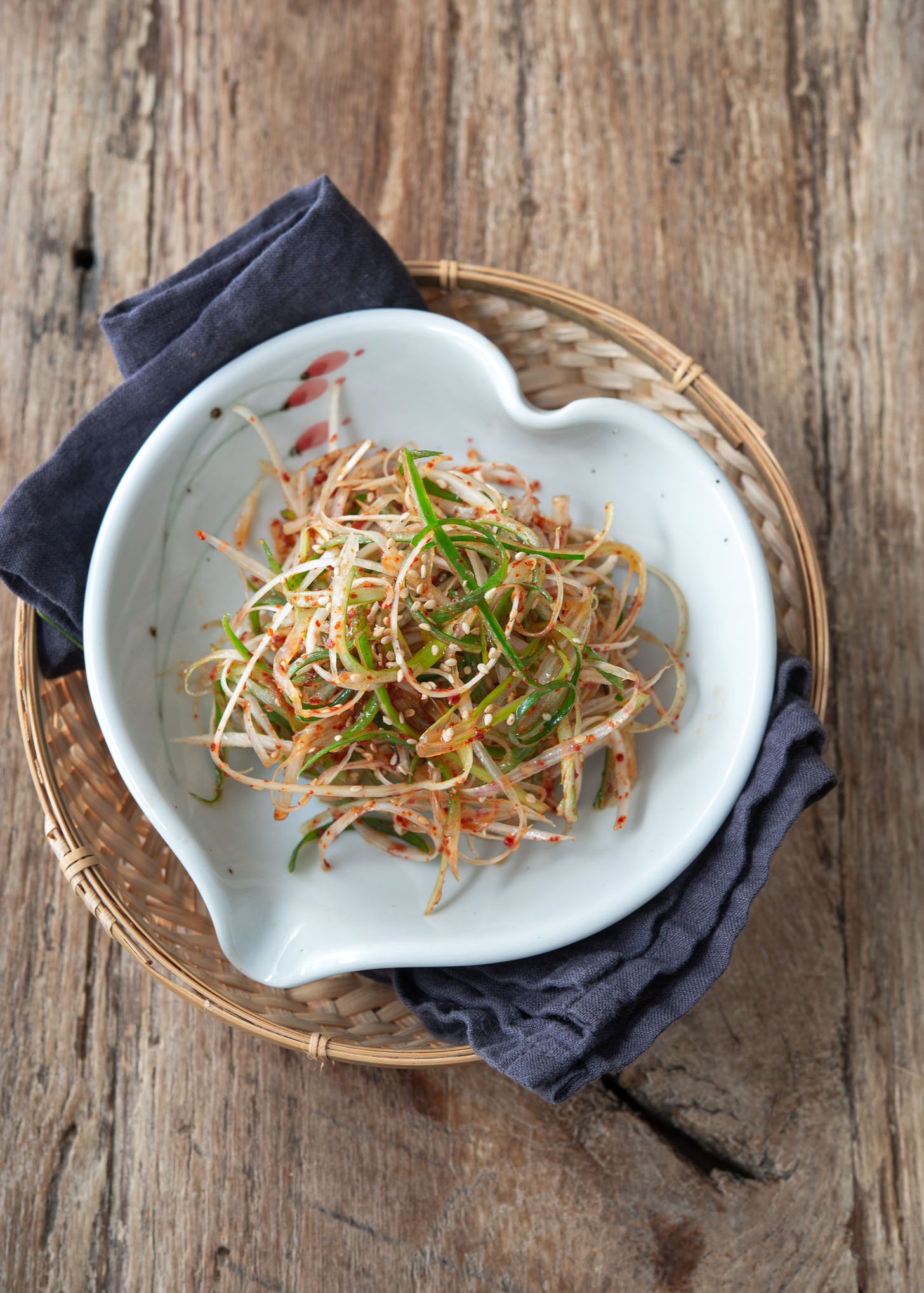 A bowl of Korean green onion salad is placed on a blue napkin.