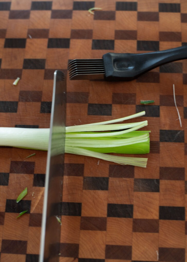 A knife is cutting off a portion of shredded green onion.