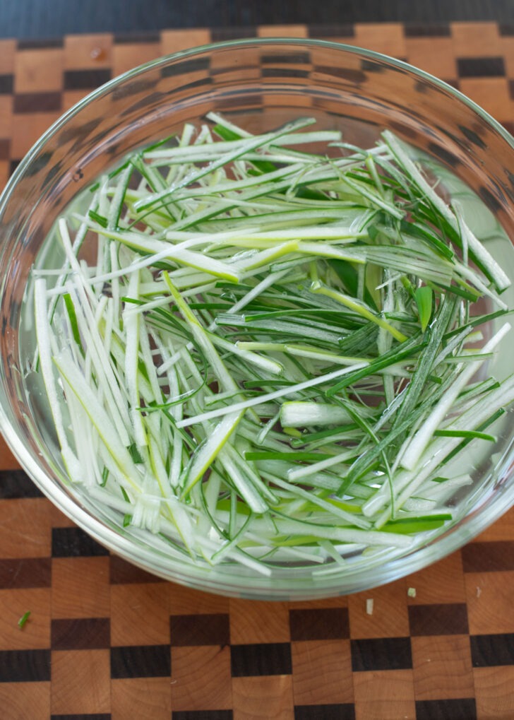 Shredded green onion is soaking in cold water in a bowl.