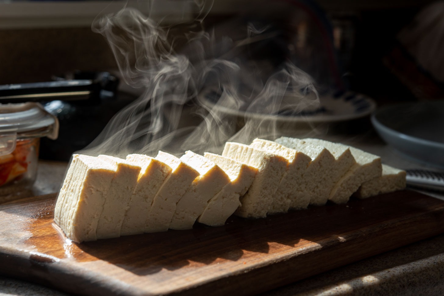 Boiled hot tofu is sliced on a cutting board.