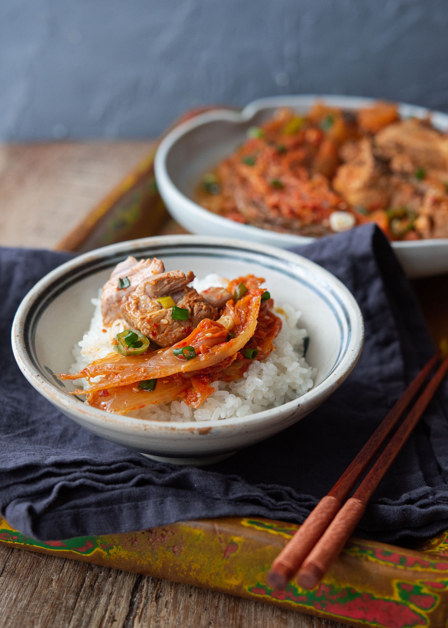 A bowl of rice is topped with pieces of kimchi jjim and a pork rib.