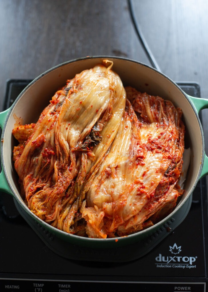 Whole cabbage kimchi is placed on top to cover the pork in a pot.