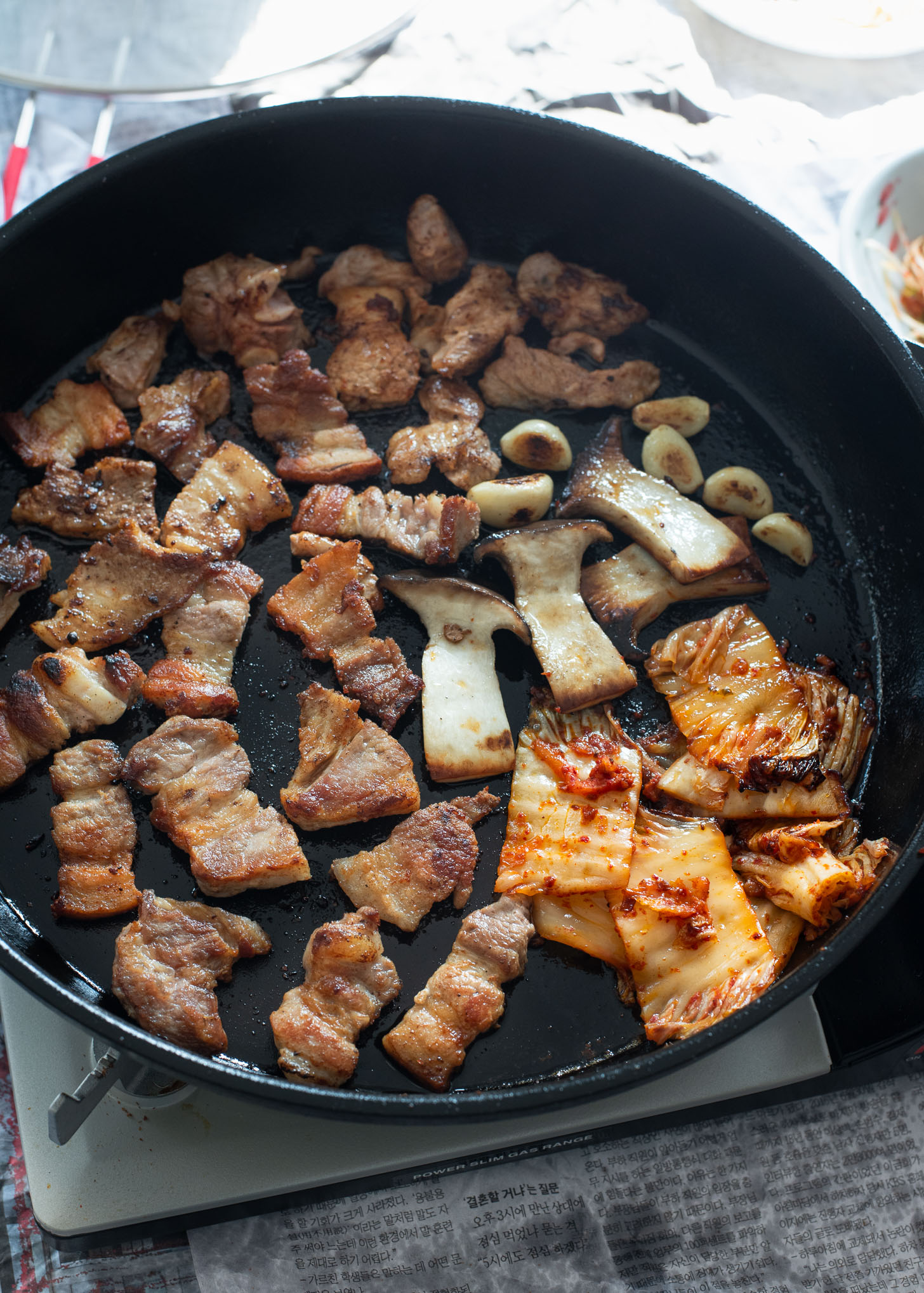 Korean pork belly is grilled with mushroom, garlic, and kimchi in a grill pan.