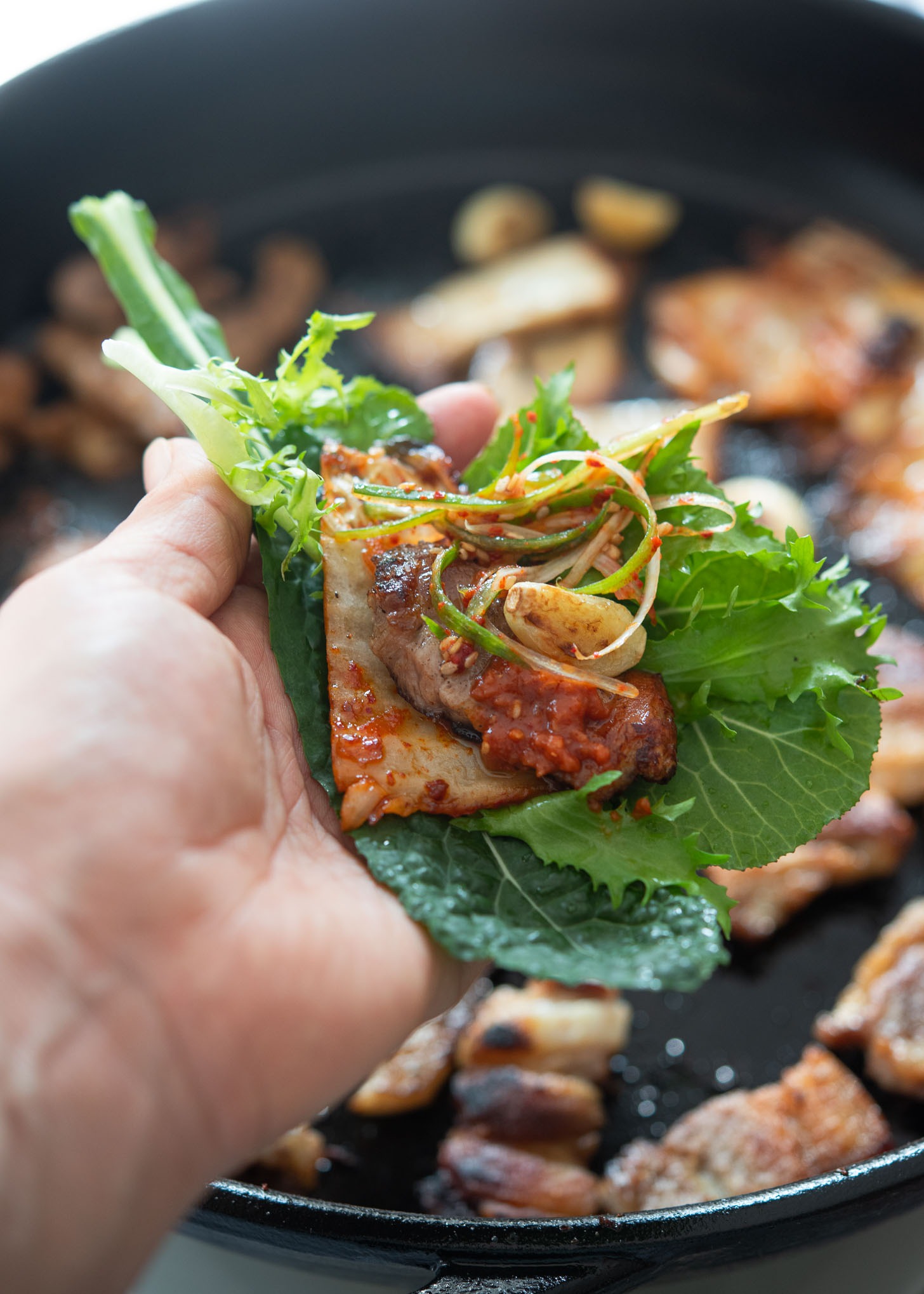 A Korean lettuce wrap filled with meat and condiments is placed on hand.