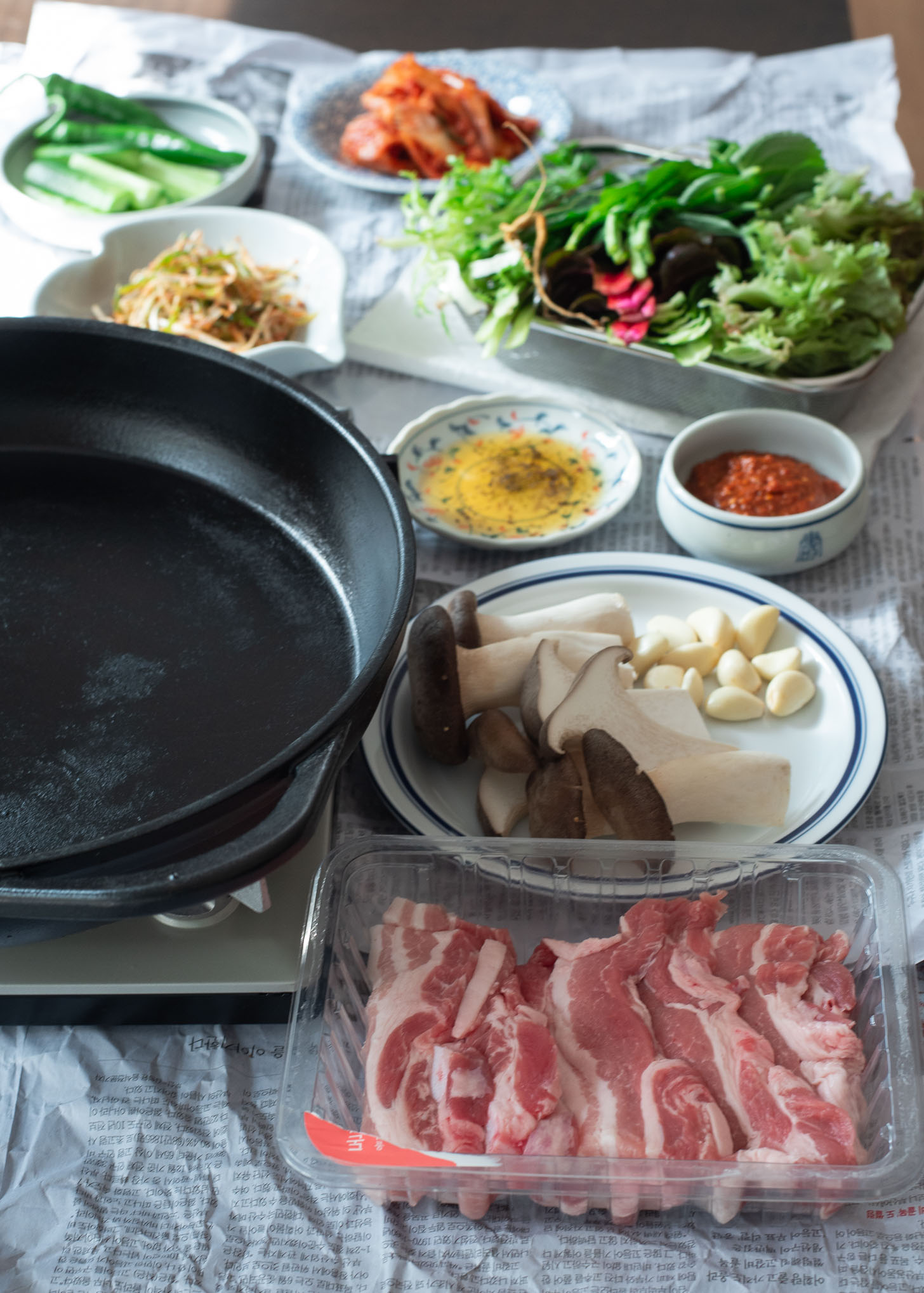 A large grill pan is placed on a table along with pork and side dishes around.