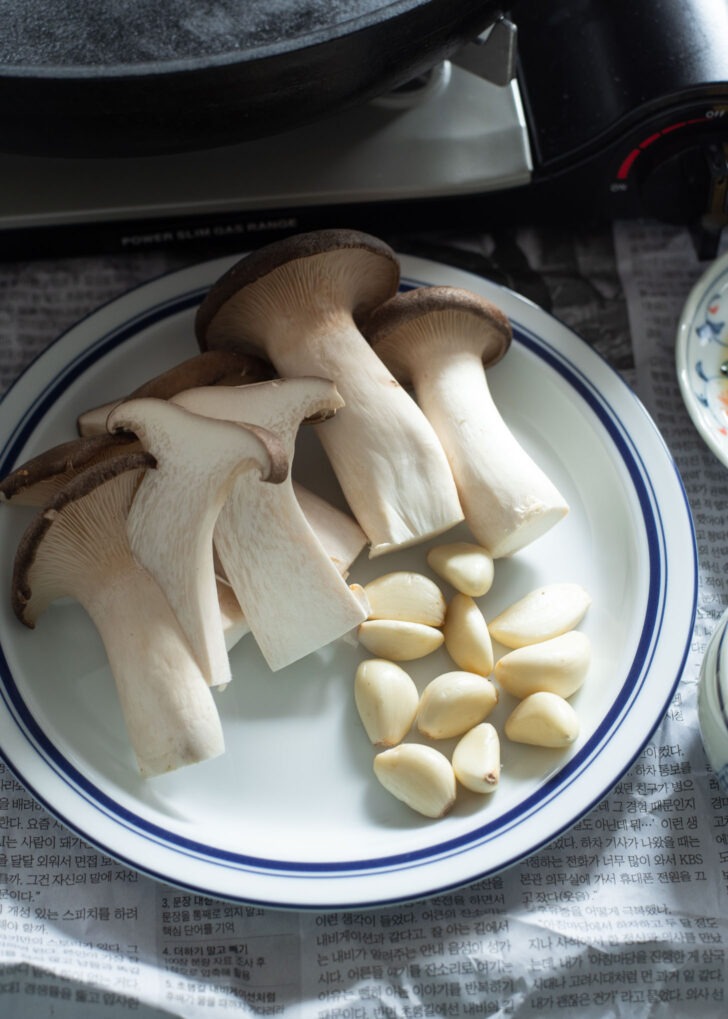 Mushroom and garlic are on a plate ready to grill.