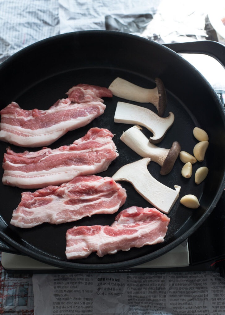 Pork belly, mushroom, and garlic is placed on a tabletop grill to make Korean BBQ.