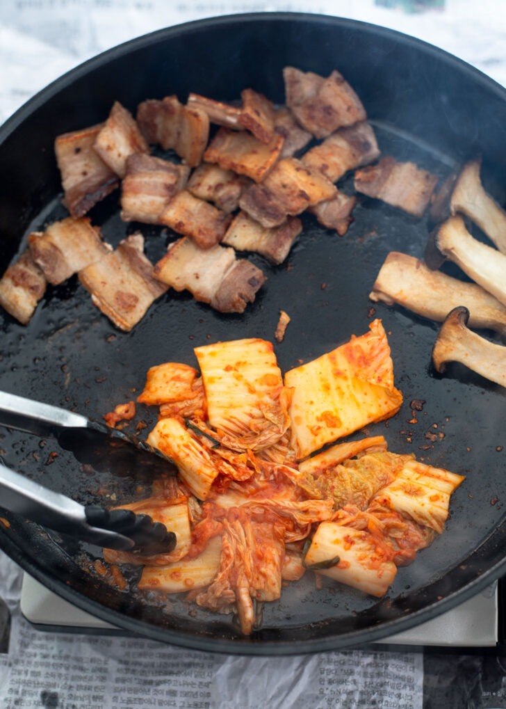 Slices of kimchi is being fried in a grill with pork belly fat.