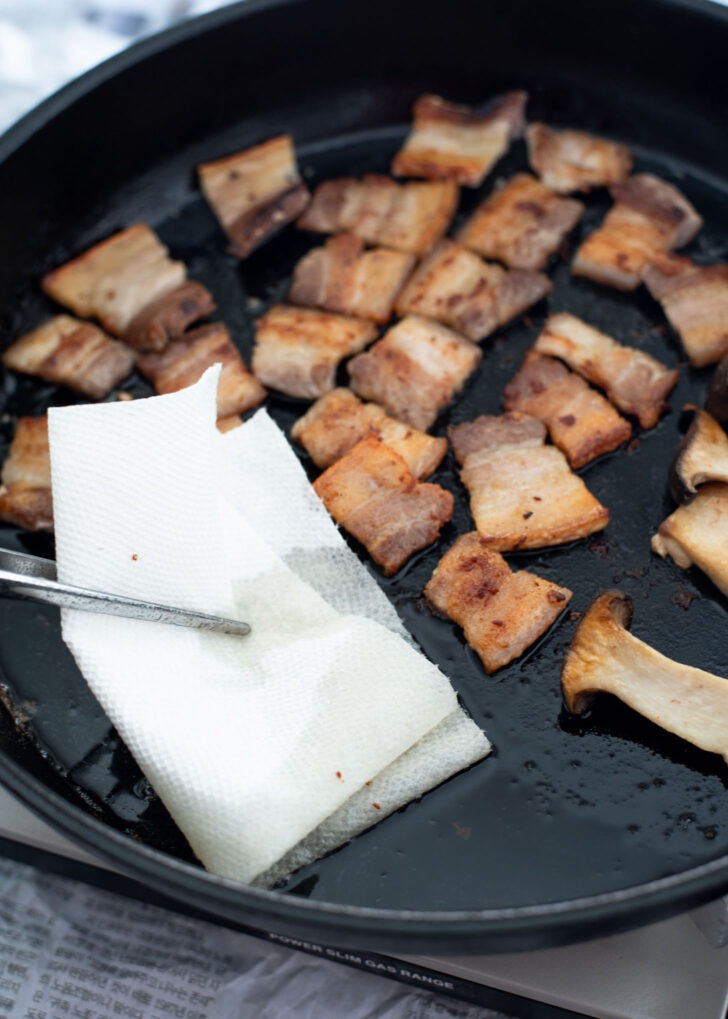 A piece of paper towel is used to wipe off the excess oil from the pork belly in grill.