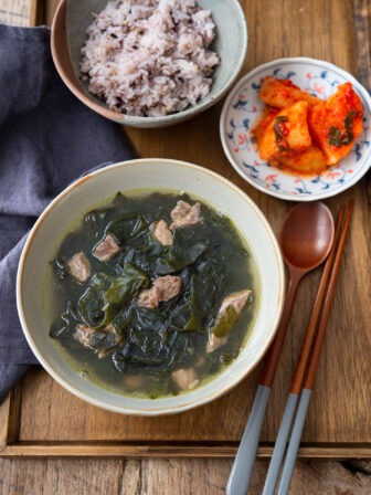 A bowl of seaweed soup is served with rice and kimchi on a tray.