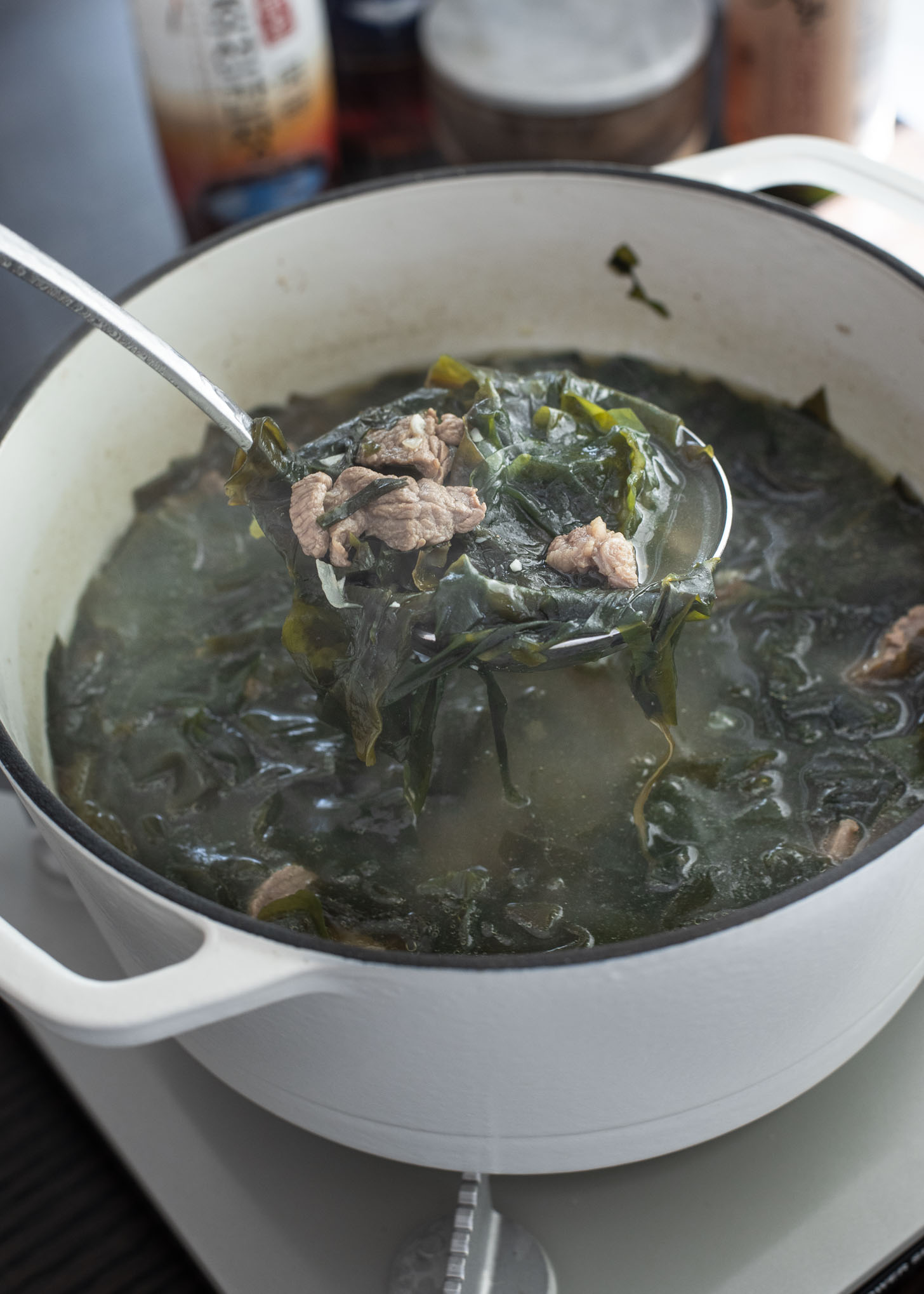 A ladle of seaweed soup with beef is lifted up from the pot.