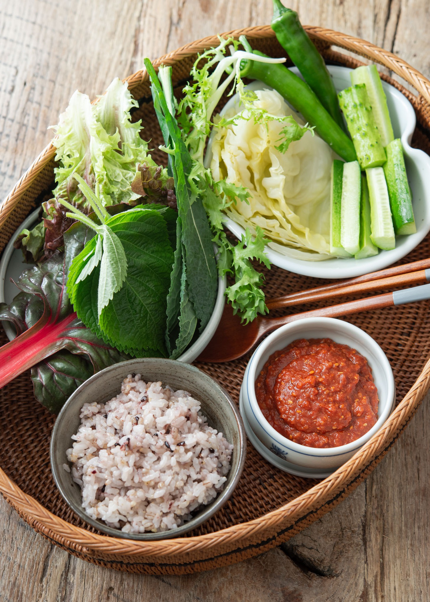 A basket ifilled with various lettuce, vegetables and ssamjang sauce with rice.