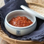 A bowl of ssamjang is presented with a lid on the side.