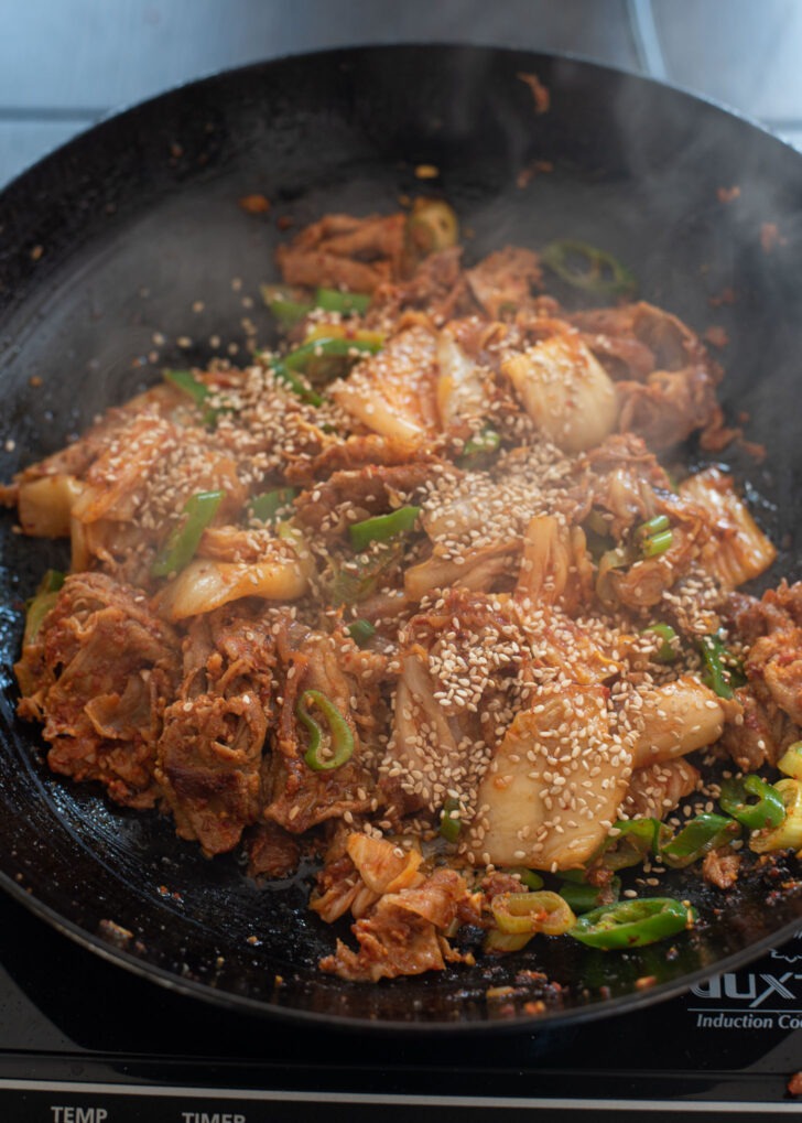 Green chili, sesame oil, and sesame seeds are added to pork kimchi stir-fry.