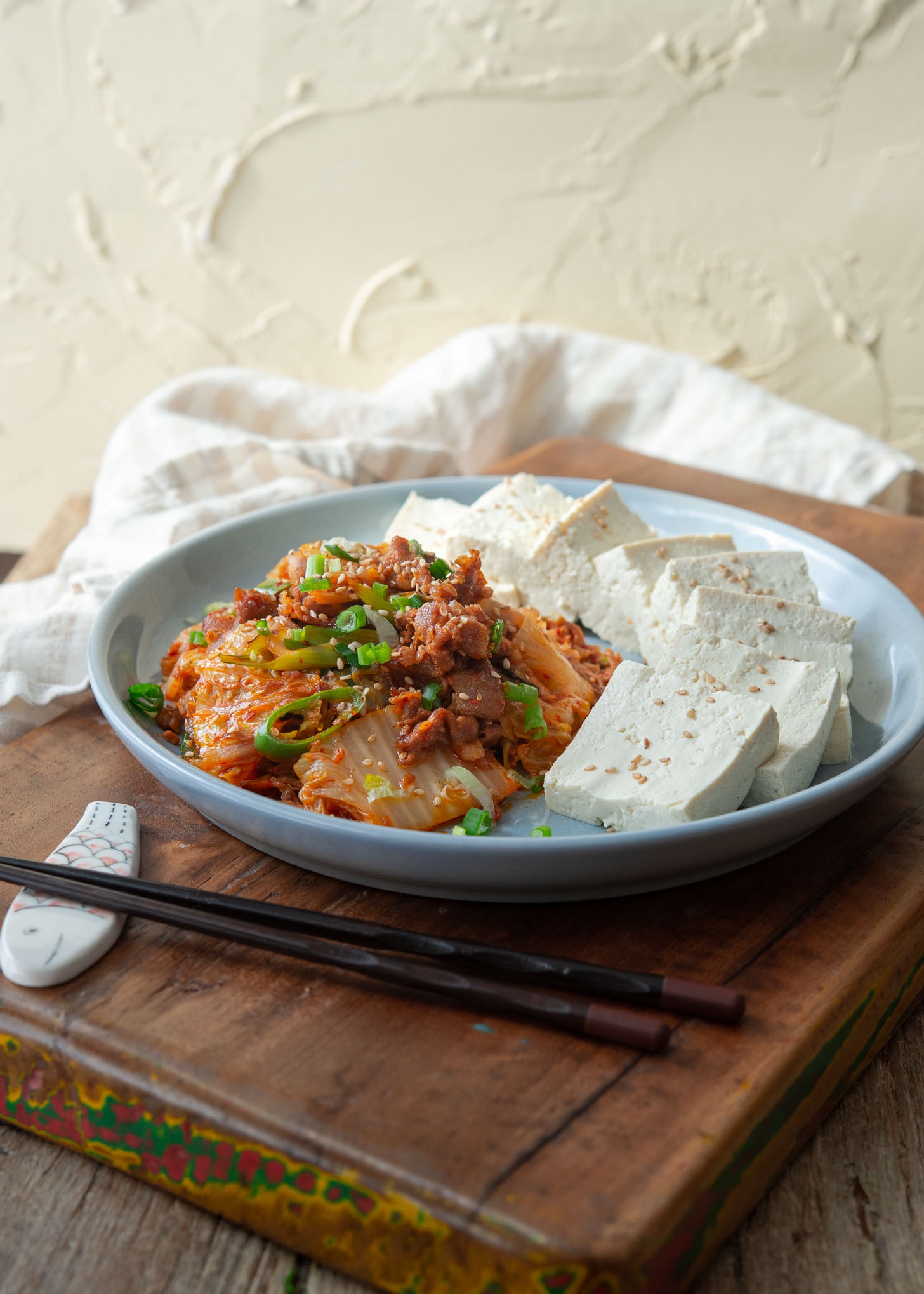 Slices of Korean boiled tofu is served with stir fried kimchi and pork on a plate.