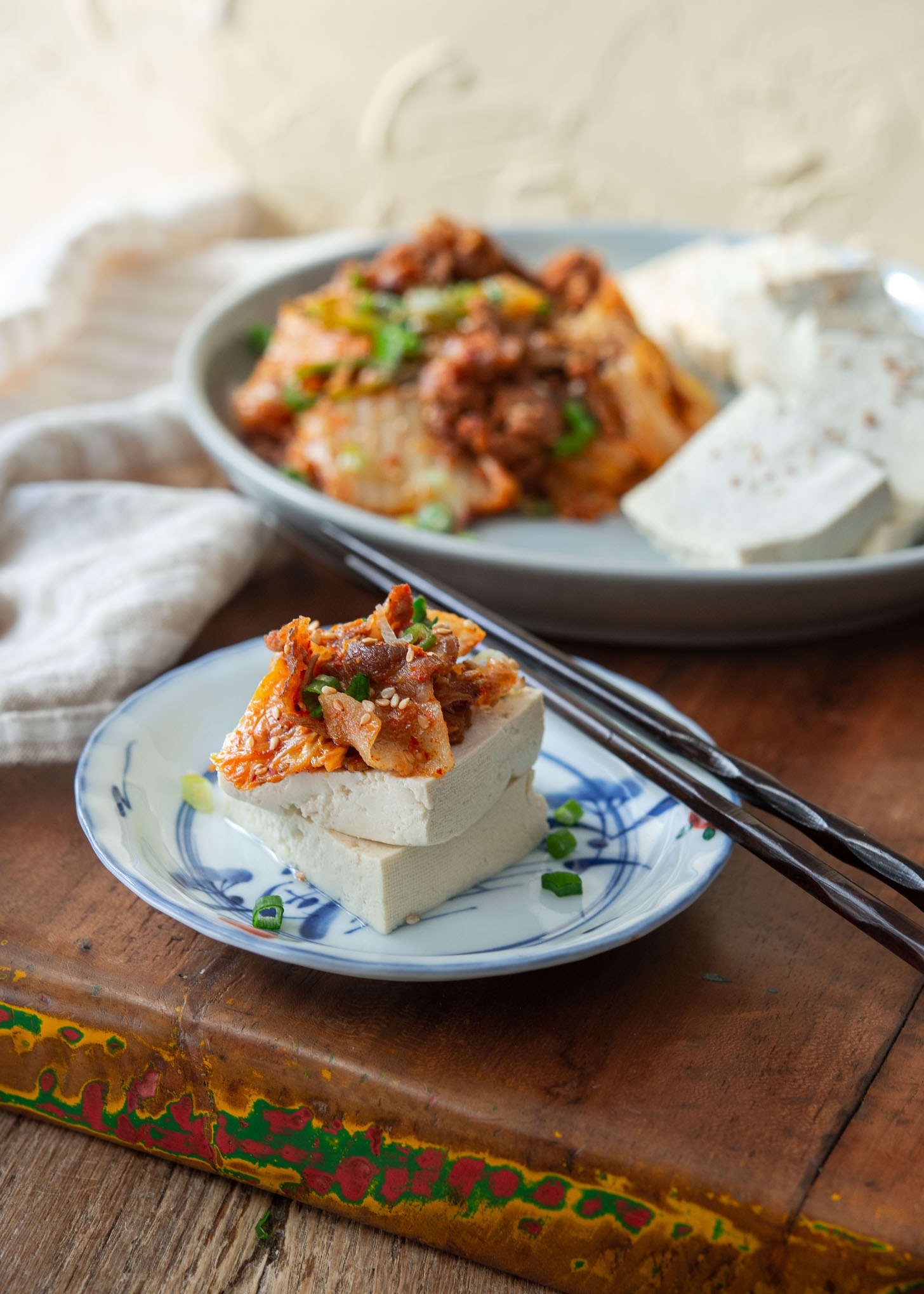 Kimchi and pork stir-fry is topped over a tofu slice on a small plate.