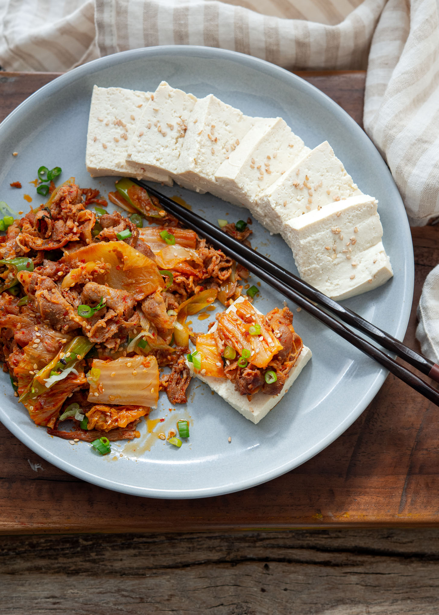 Tofu slices and kimchi pork stir fry is arranged on a serving plate.