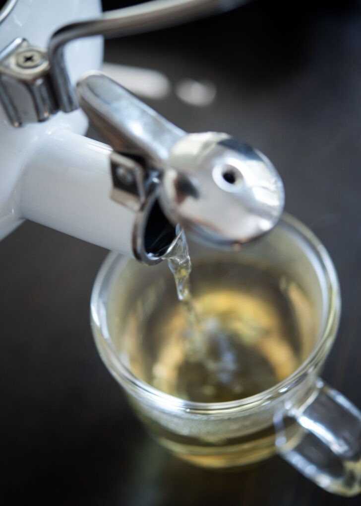 A kettle pouring boiling hot barley tea to a cup.