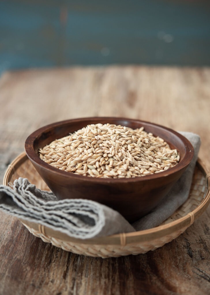 Whole, unhulled barley grains are placed in a wooden bowl.